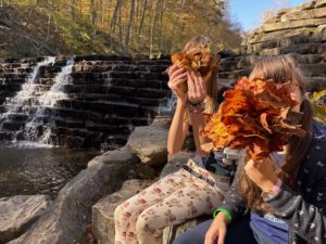 Sarah and Amy holding leaf bouquets in front of their faces near a waterfall