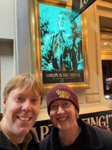 Carl and Jenny in front of a poster for the musical Swept Away