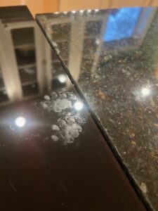 A black stovetop reflecting ceiling lights around two distinct greasy cat paw prints.